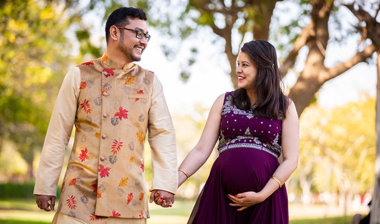 A young man and a young pregnant woman dressed in festive wears walking happily